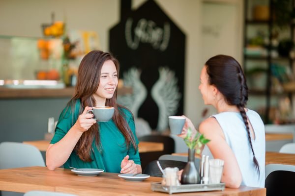 Happy smiling young women with coffee cups at cafe
